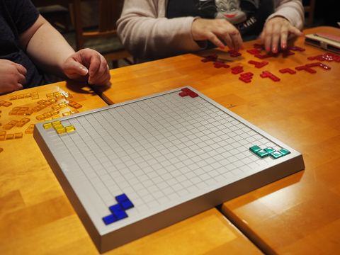 A four-player game of Blokus just after the game start at a special board game camp in Tampere, Finland. All four players have only placed a single tile so far. According to the rules, each player's first tile must touch the corner of the board.