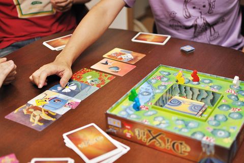 A game of Dixit in progress. Six cards have been dealt out and voted on, and the storyteller is indicating which story belonged to them. To the right, scores are tracked by rabbit-shaped tokens on a scoring track